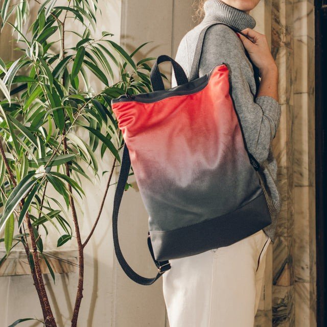 1. Woman wearing Muni salmon faux leather backpack indoors near plants and wooden paneling