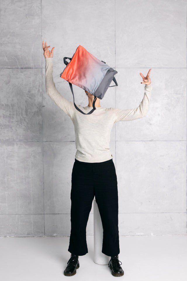 1. Person playfully holding Muni salmon faux leather backpack in front of face against grey wall