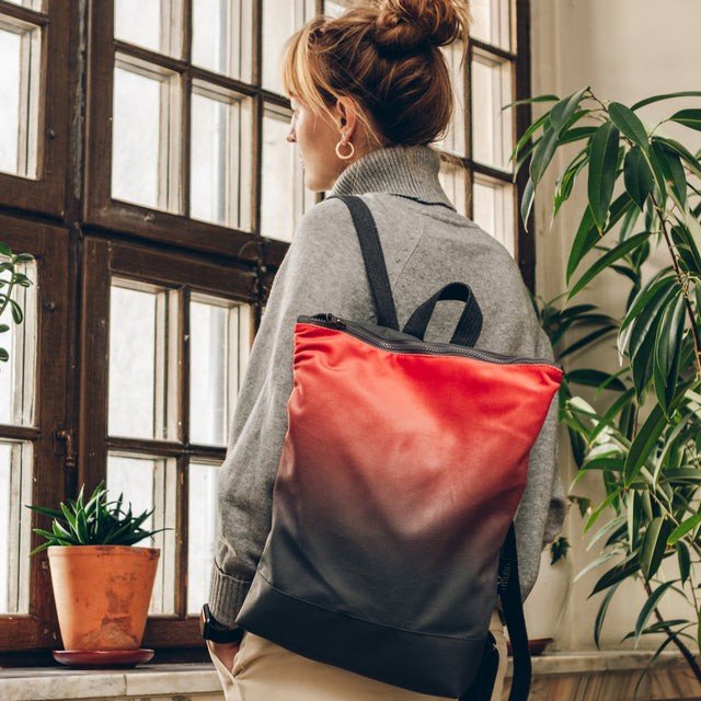 1. Woman wearing Muni salmon faux leather backpack looking out window with plants in background