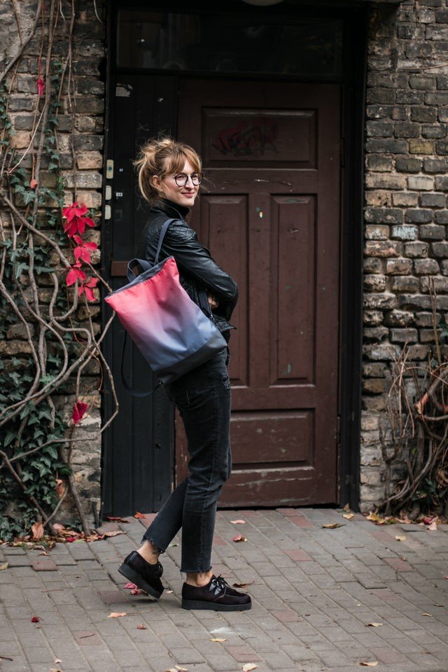 1. Woman wearing Muni salmon faux leather backpack walking on cobblestone street with brick wall background