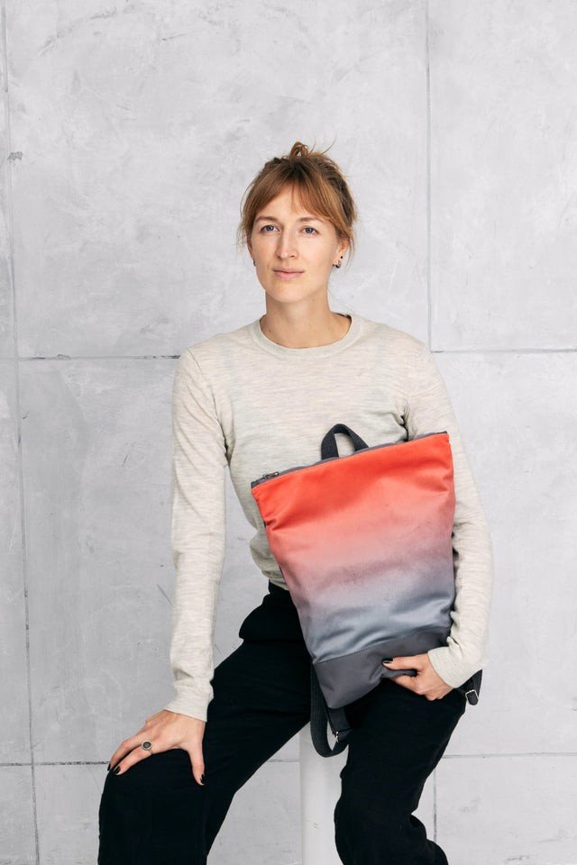 1. Woman sitting holding Muni salmon faux leather backpack against grey wall