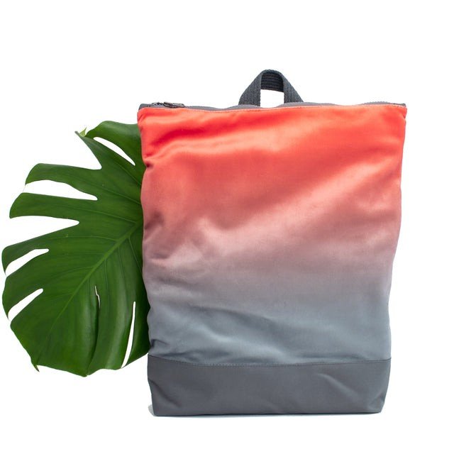 2. Muni salmon faux leather backpack with grey bottom next to large green leaf in studio setting