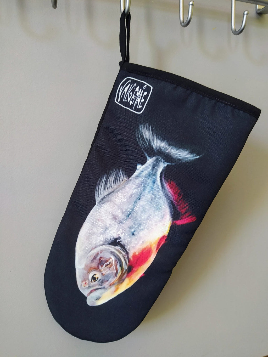 7. Black oven mitt with fish painting hanging on wall, highlighting artistic design and brand logo