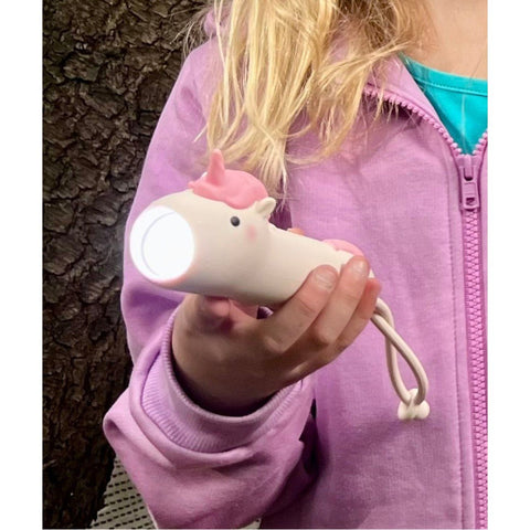 1. Child holding illuminated pink unicorn-shaped flashlight, wearing a purple jacket, standing outdoors