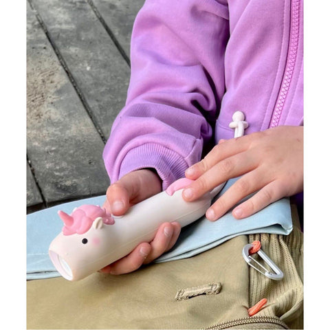 1. Child holding pink unicorn-shaped flashlight while sitting outdoors, wearing a purple jacket