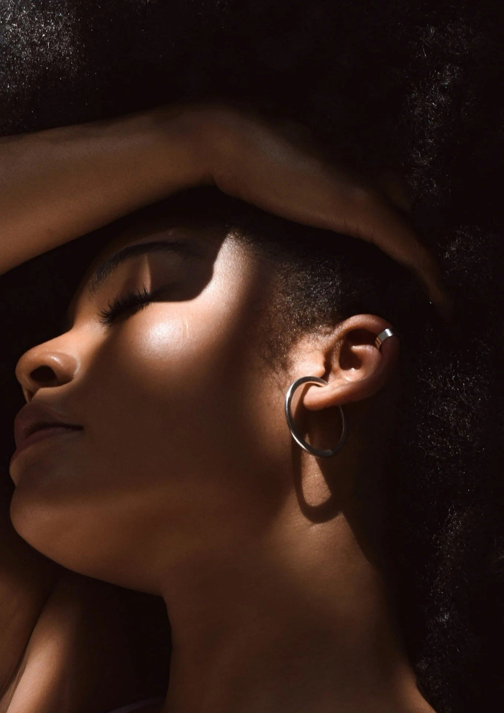 5. Close-up of woman wearing NO MORE Flat Upper Ear Cuff in silver, paired with large hoop earrings, in a shadowed lifestyle setting
