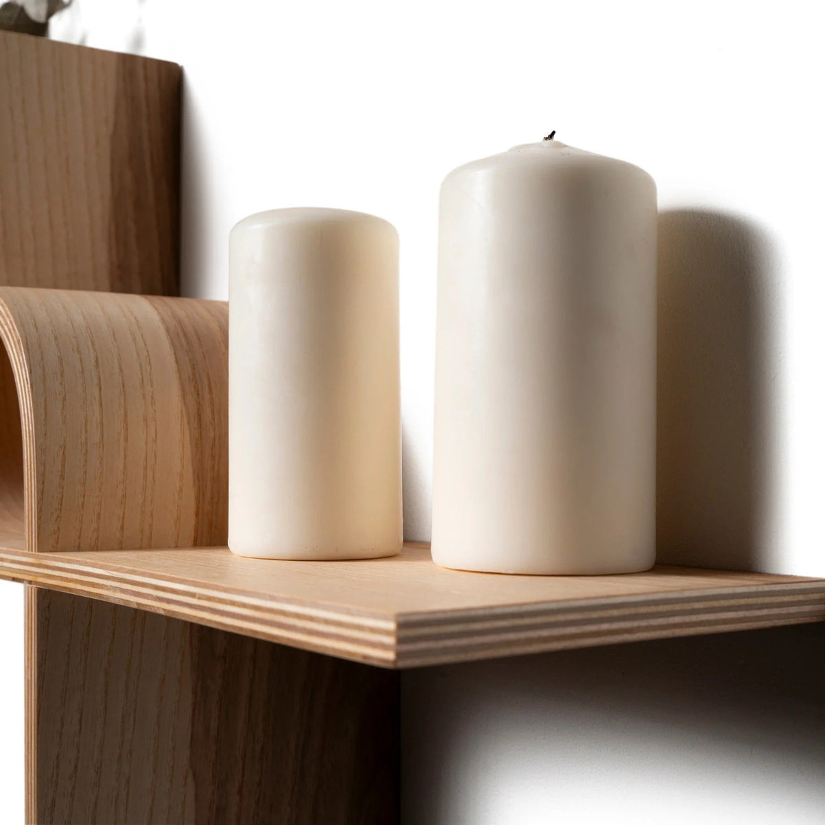 6. Close-up of two white candles on wooden floating shelf, highlighting smooth finish