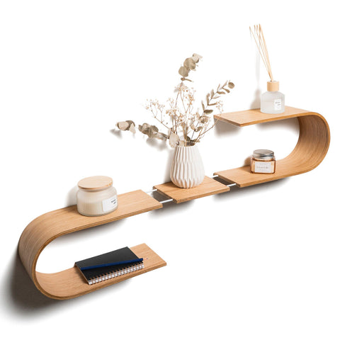 1. Wave-shaped floating wooden wall shelf with decor items including a vase with dried flowers and candles, made from Baltic birch plywood, mounted on a white wall.