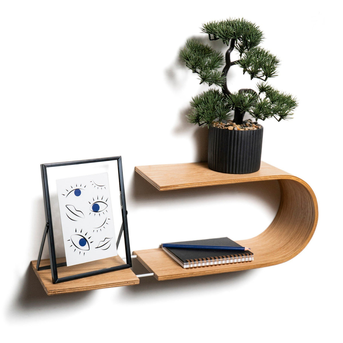 3. Wooden wall shelf with a bonsai plant and framed artwork, featuring a wave design, made from Baltic birch plywood, mounted on a white wall.