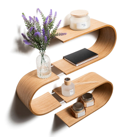 2. Angled view of S-shaped floating wooden wall shelf with decor items like a vase, candles, and a notebook, crafted from baltic birch plywood by Ewart Woods