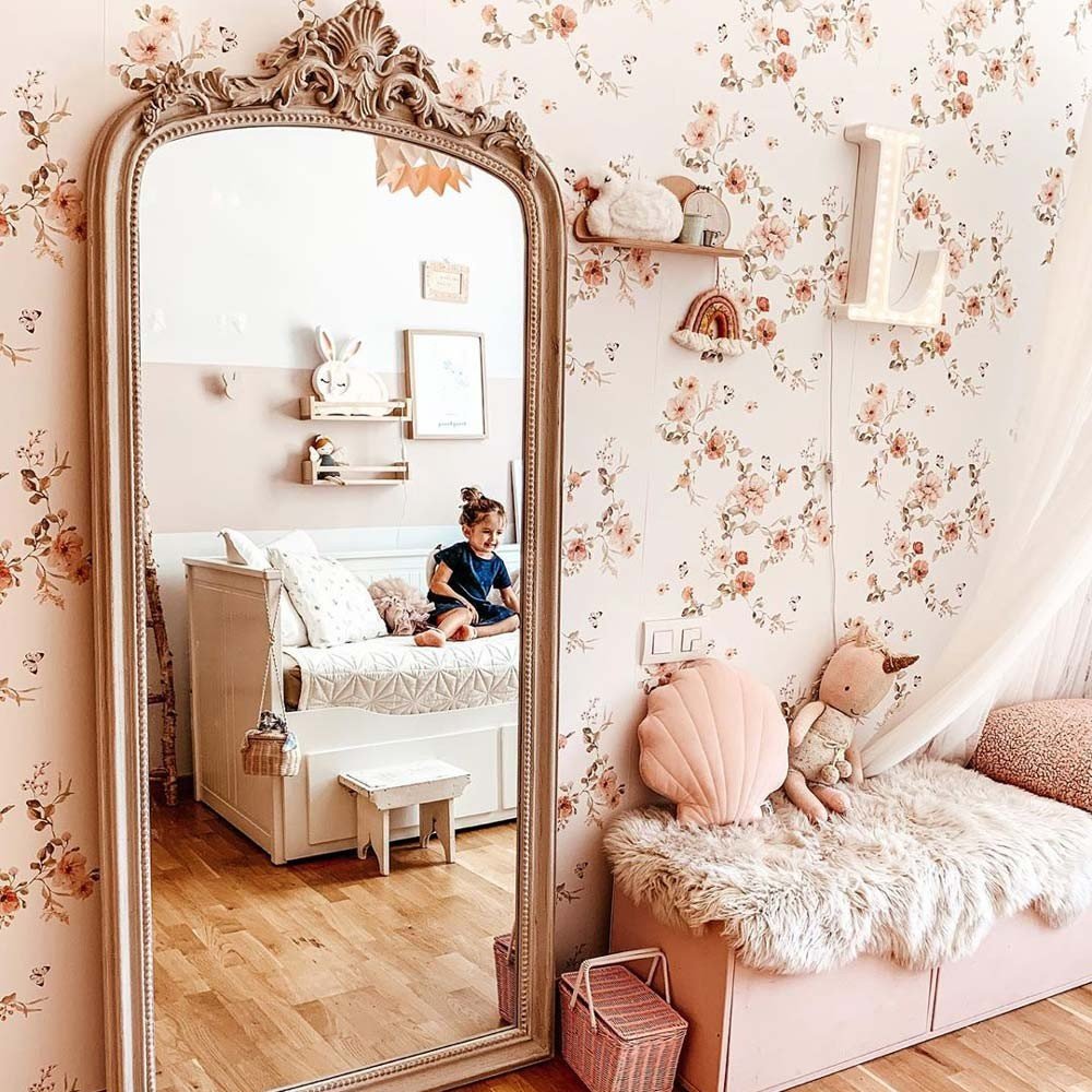 9. Girl sitting on bed in room with floral vintage wallpaper, large mirror, and plush decor