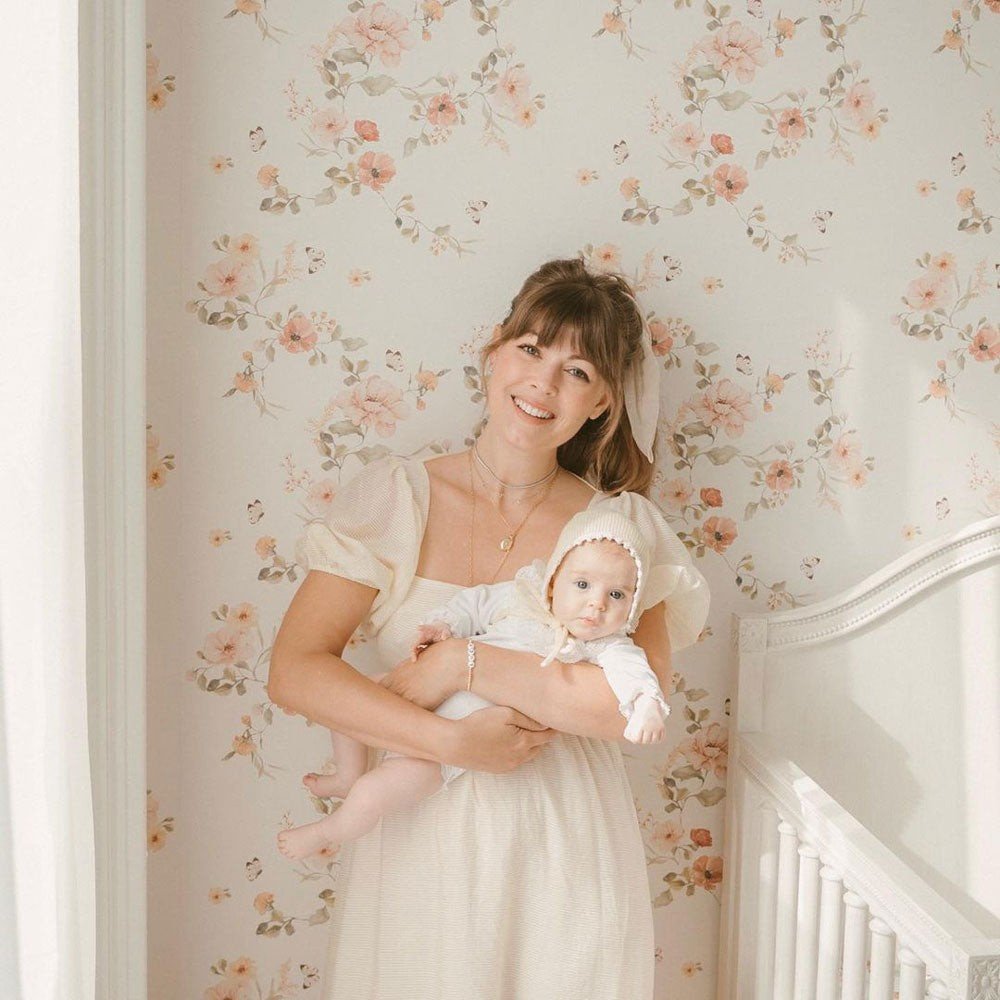 3. Woman holding baby in front of floral vintage wallpaper, both wearing light-colored clothing