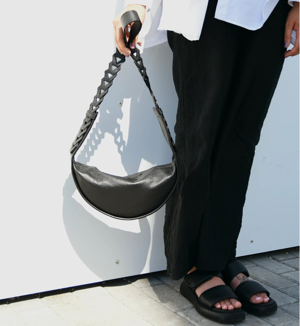 1. Woman holding black Flora Leather Bag by Gerda Retter Design, showcasing crossbody style in outdoor setting