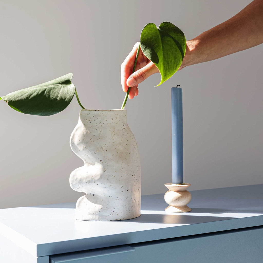 3. Lifestyle image of a hand placing a leaf in the white Fluxo Ceramic Vase by 5mm Paper, next to a blue candle