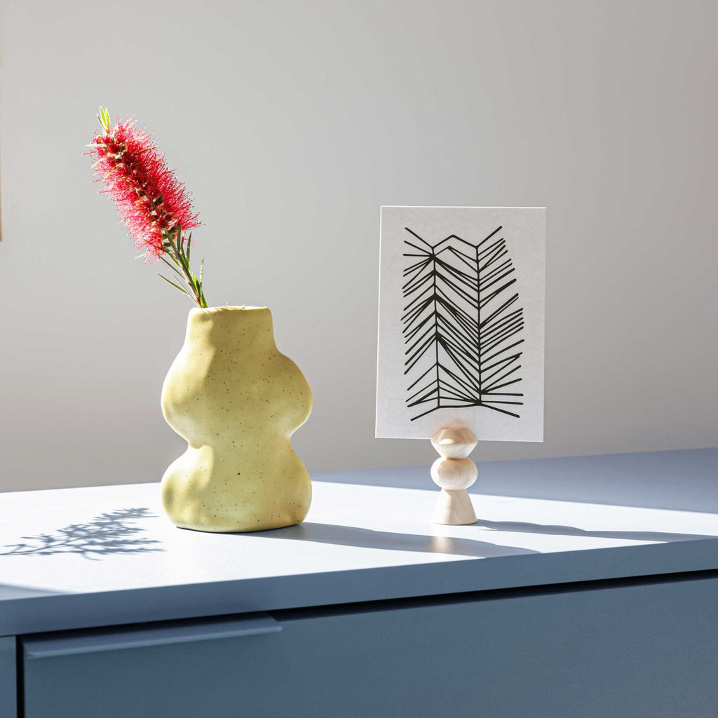 4. Lifestyle image of Fluxo Ceramic Vase in pistachio with a red flower, next to a decorative card