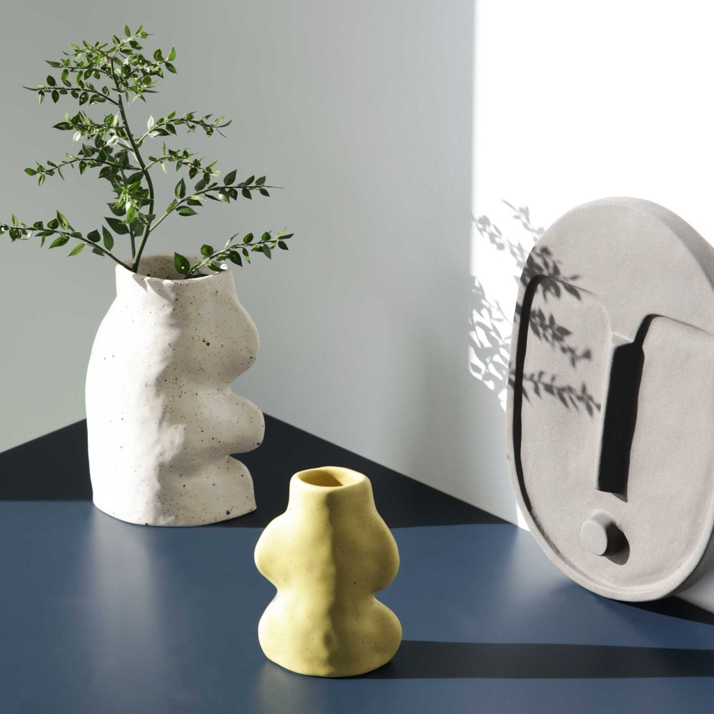 3. Lifestyle image of Fluxo Ceramic Vase in pistachio with a plant, next to a white vase and wall art