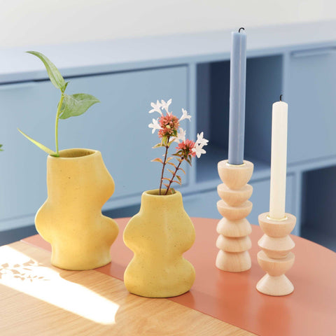 2. Lifestyle image of two Fluxo Ceramic Vases in pistachio with flowers, alongside wooden candle holders