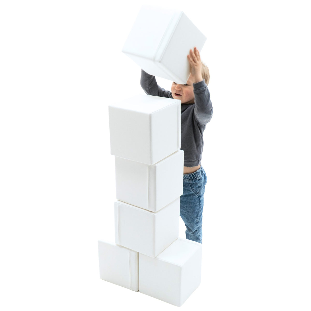 7. Child in grey sweater and blue jeans stacking white foam building blocks into a tall tower