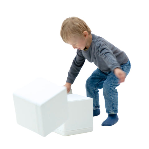 2. Child in grey sweater and blue jeans playing with white foam building blocks on a white background
