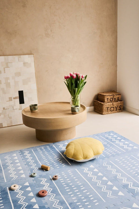 2. Blue OLYA KIDS Boho puzzle playmat in living room with round wooden table, tulips, and toy storage