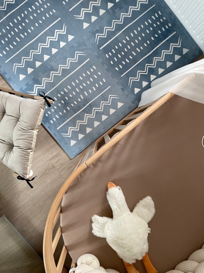 4. Overhead view of blue OLYA KIDS Boho puzzle playmat next to crib and plush toy