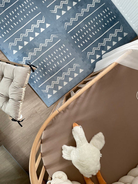 4. Overhead view of blue OLYA KIDS Boho puzzle playmat next to crib and plush toy