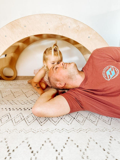1. Man and child lying on ivory and black boho playmat in cozy room with wooden arch