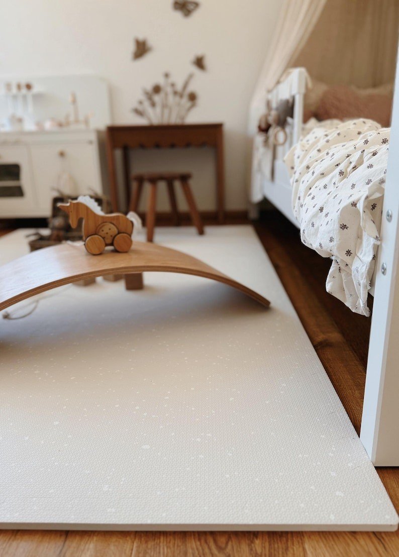 1. Cozy nursery with OLYA KIDS cashmere spots playmat on wooden floor, featuring wooden toys and a bed with floral bedding