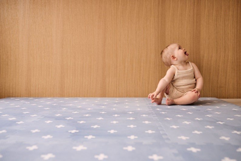 1. Baby sitting on OLYA KIDS Cross Azure foam puzzle playmat against wooden wall background