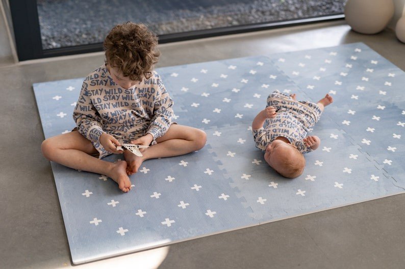 1. Two children sitting and lying on OLYA KIDS Cross Azure foam puzzle playmat wearing matching outfits