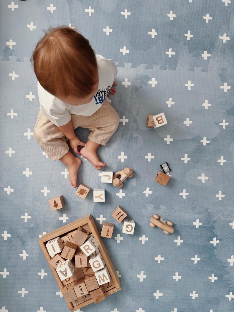 3. Overhead view of toddler playing with wooden blocks on OLYA KIDS Cross Azure foam puzzle playmat