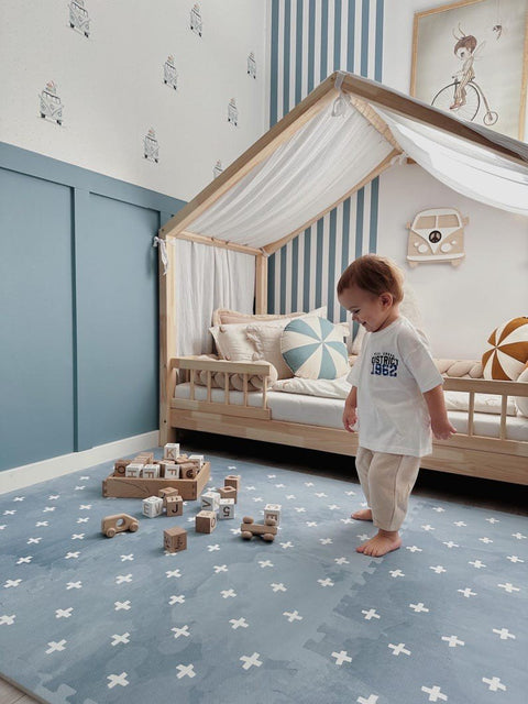 1. Toddler standing on OLYA KIDS Cross Azure foam puzzle playmat with wooden blocks in stylish nursery