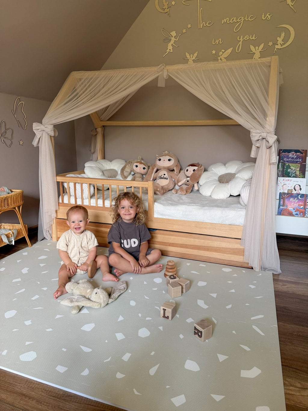 4. Two children sitting on OLYA KIDS Terrazzo Dove foam puzzle playmat in bedroom with canopy bed and toys