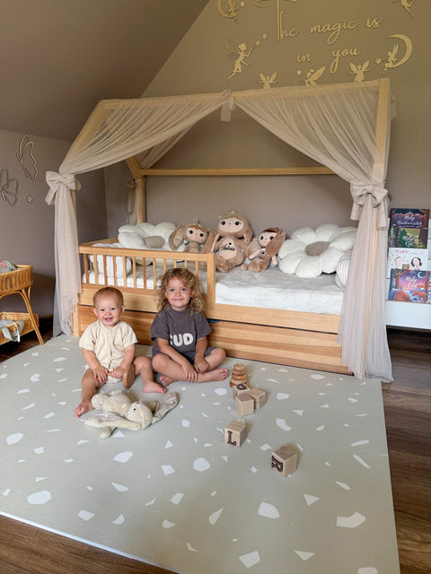 4. Two children sitting on OLYA KIDS Terrazzo Dove foam puzzle playmat in bedroom with canopy bed and toys