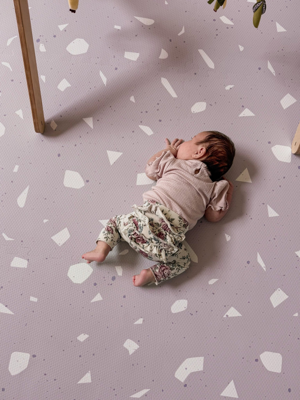 1. Baby lying on lavender terrazzo playmat with wooden play gym overhead