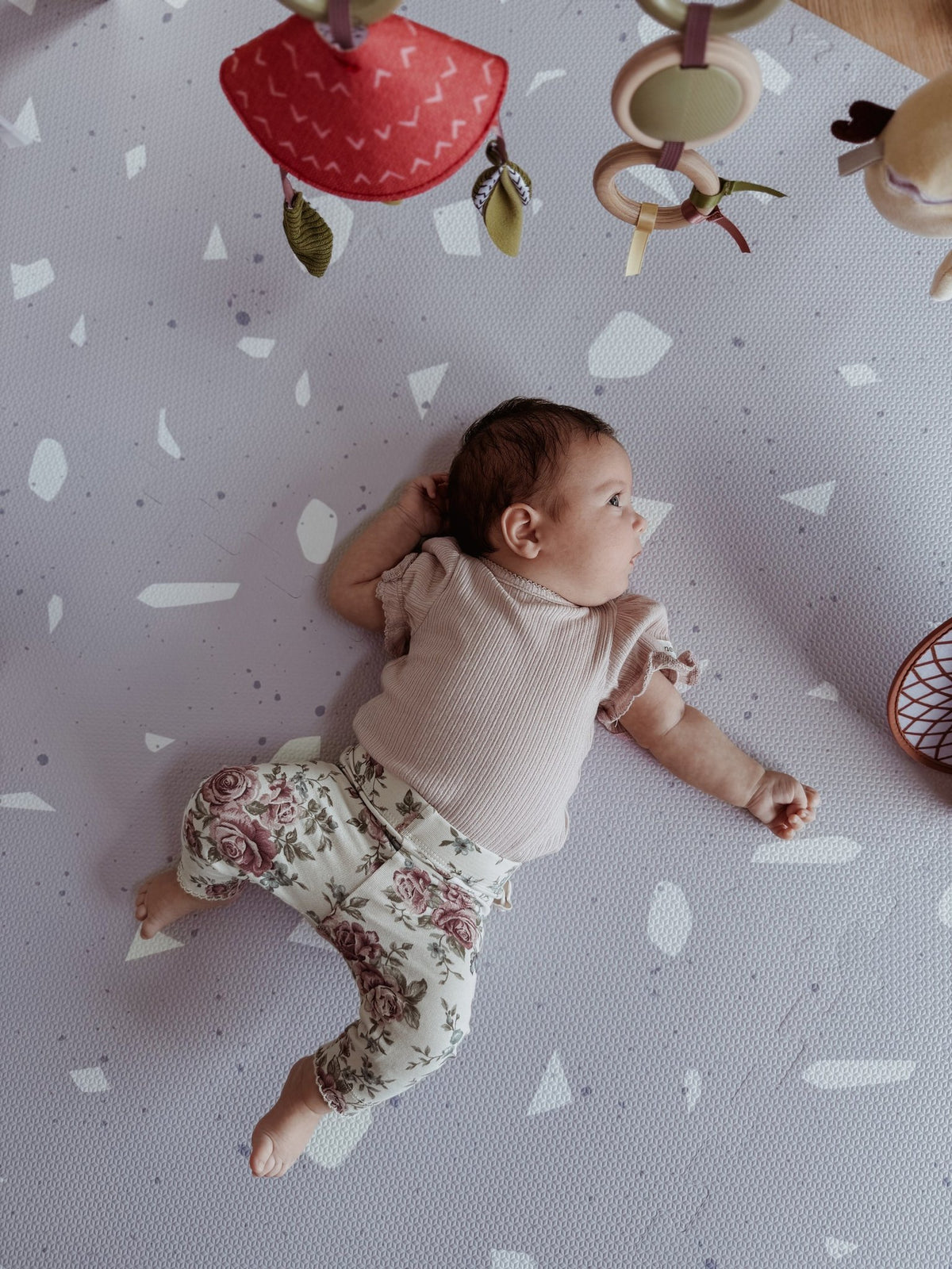 3. Baby on lavender terrazzo playmat with floral pants and toys above