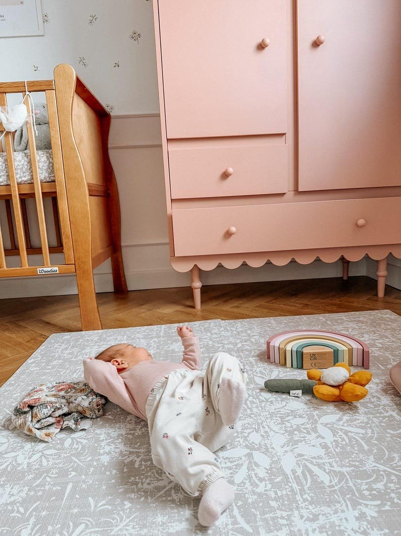 1. Baby lying on vintage beige foam puzzle playmat in nursery with pink wardrobe and toys