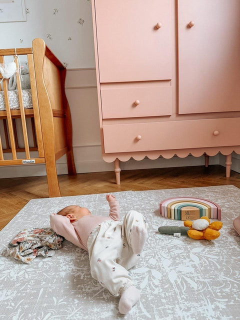 1. Baby lying on vintage beige foam puzzle playmat in nursery with pink wardrobe and toys
