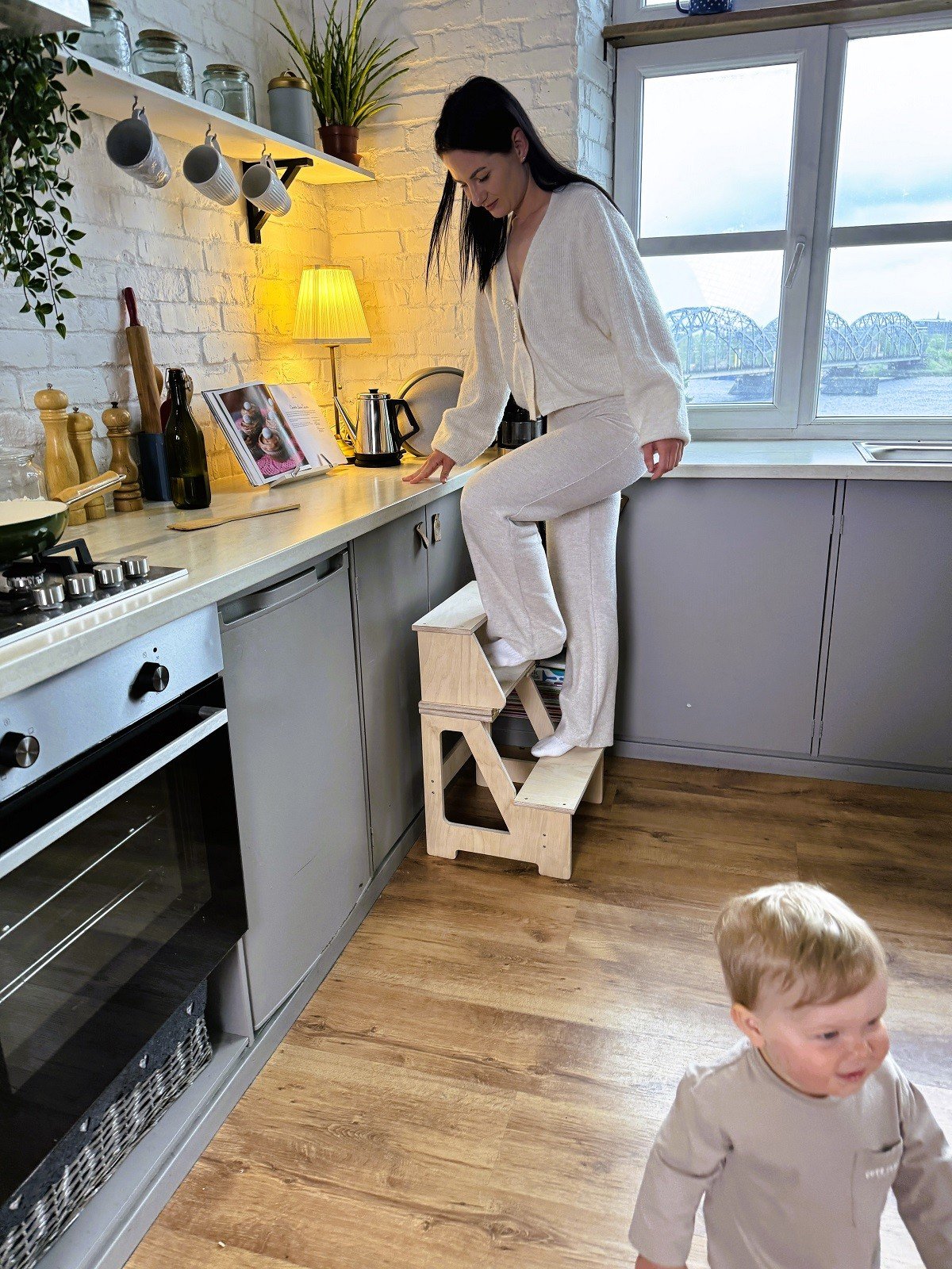1. Woman using wooden folding seat and climbing helper in kitchen with child nearby