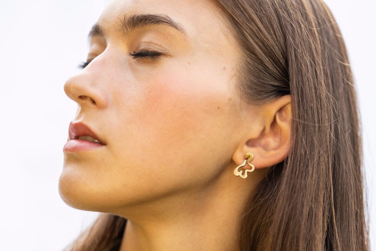 1. Side profile of woman wearing Lentsius Folia Mini Earrings in gold-tone, eyes closed, against light background
