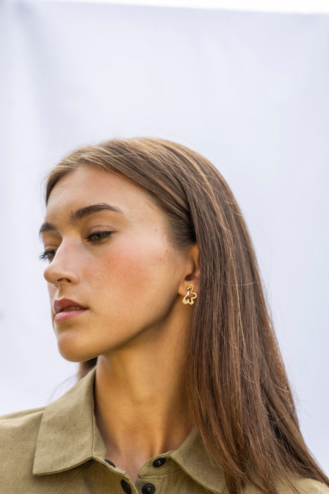1. Woman in side view wearing Lentsius Folia Mini Earrings in gold-tone, light background