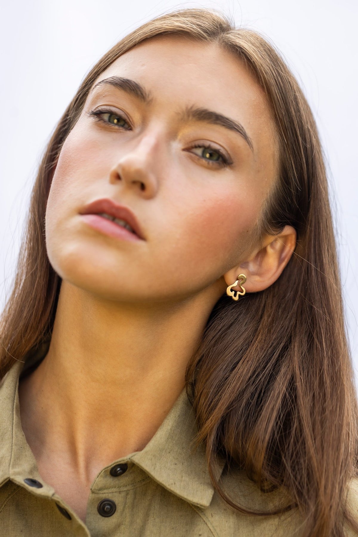 1. Woman wearing Lentsius Folia Mini Earrings in gold-tone, close-up with neutral expression and light background