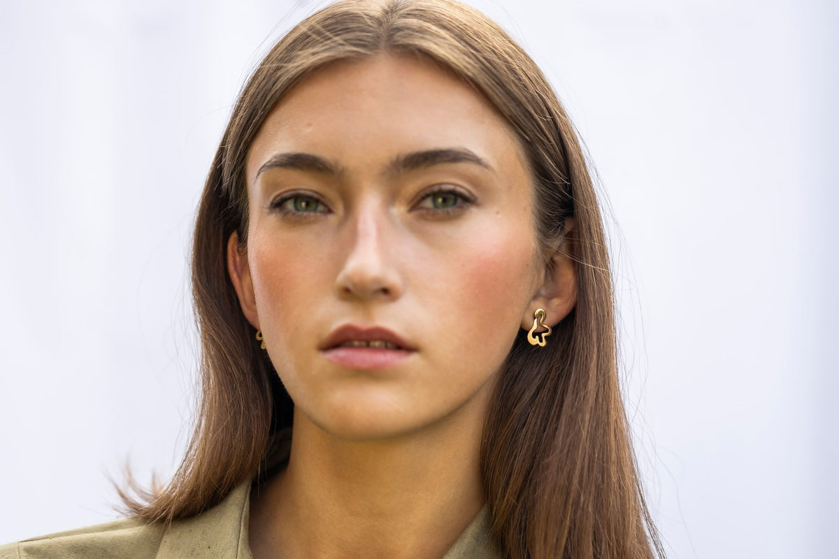 1. Woman facing forward wearing Lentsius Folia Mini Earrings in gold-tone, light background