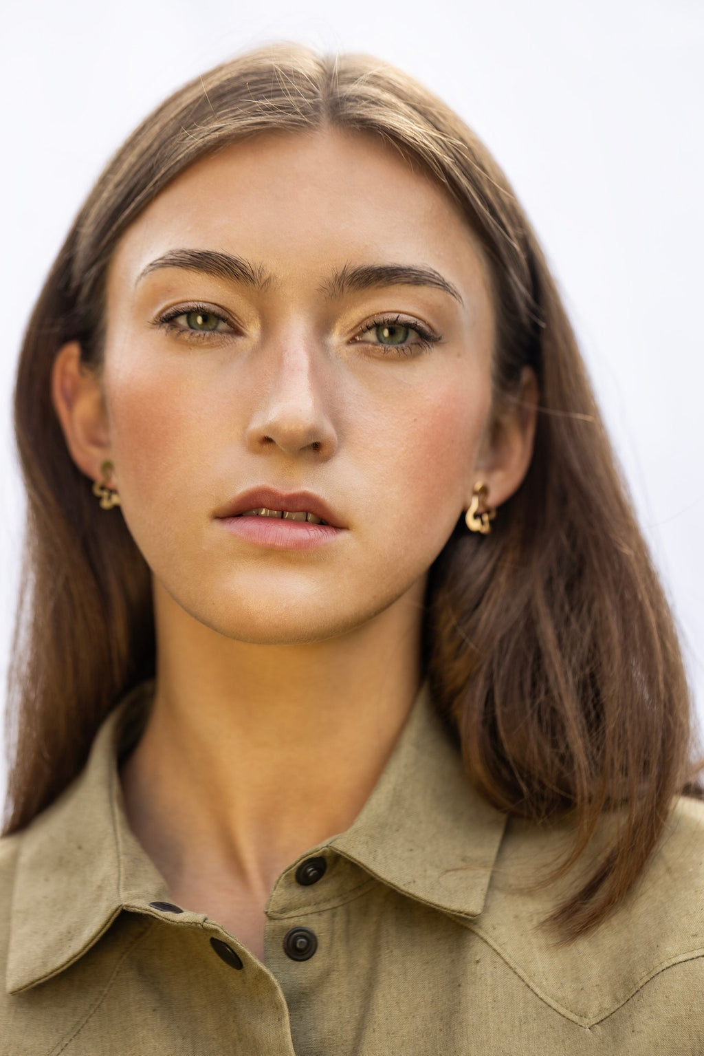 1. Woman facing forward wearing Lentsius Folia Mini Earrings in gold-tone, neutral expression, light background