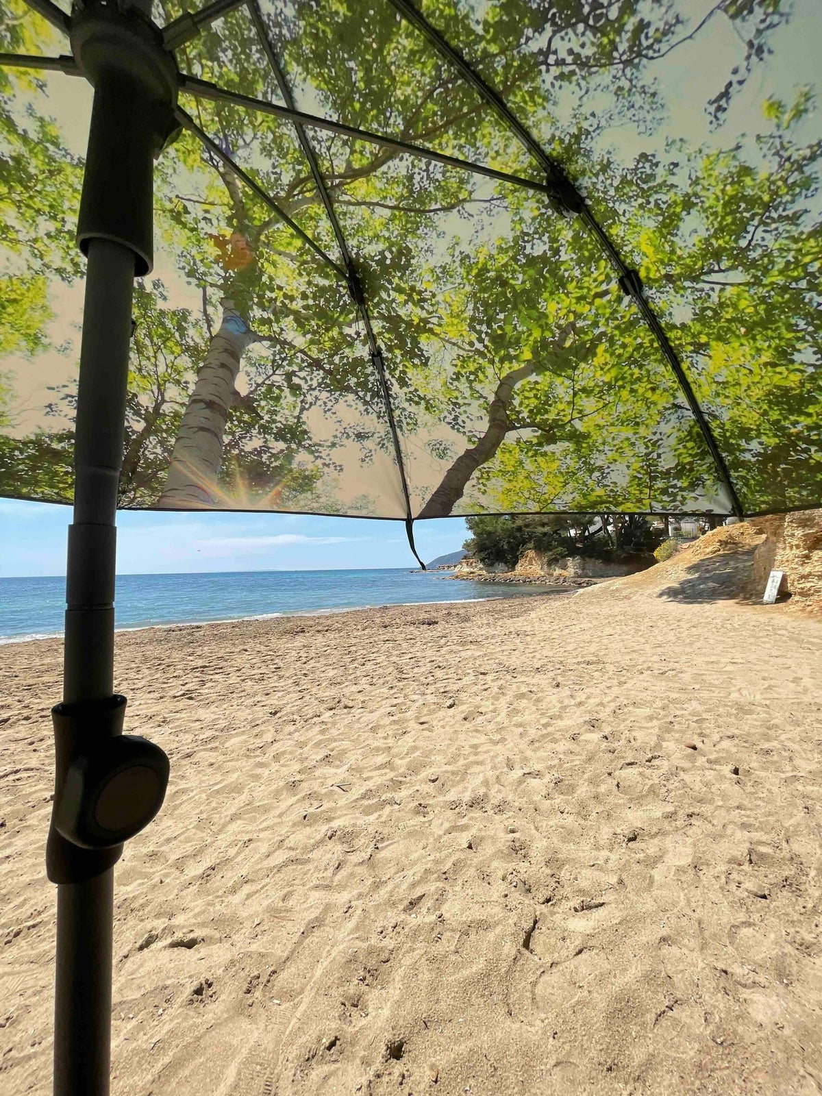 1. Beach view from under HAPPYSWEEDS forest-themed parasol with tree canopy print, providing shade on sandy shore