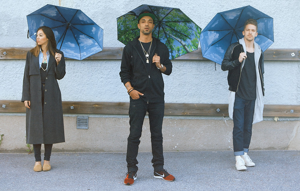 1. Three people standing with forest print umbrellas against urban wall