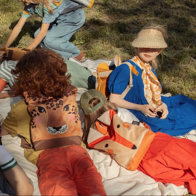 11. Muni fox backpack on picnic blanket with children, showcasing playful outdoor setting
