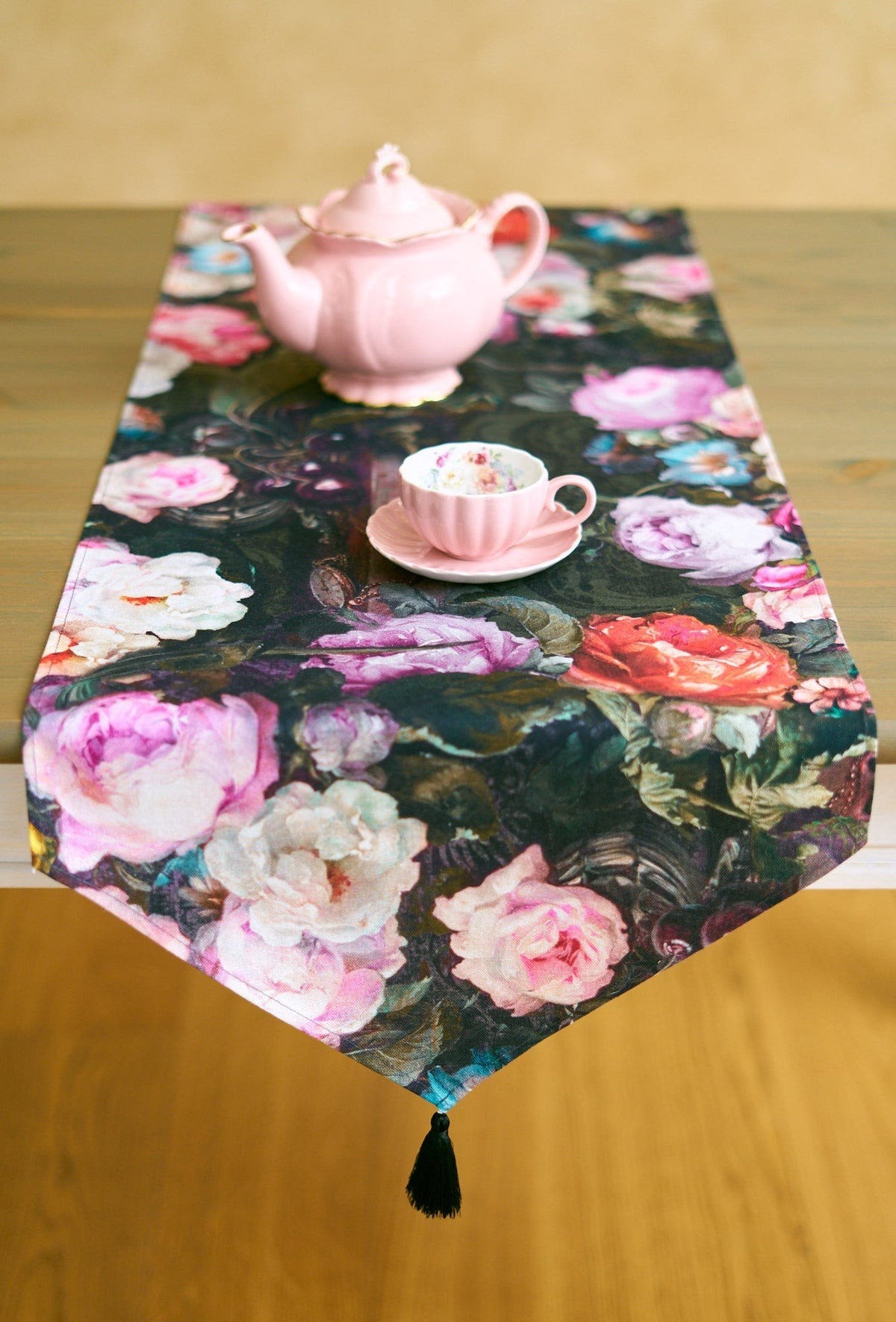 1. Francine black table runner with floral pattern and tassels on wooden table with pink teapot and cup