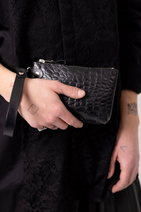 1. Person holding black alligator leather POUCH wallet with wrist strap, wearing black clothing