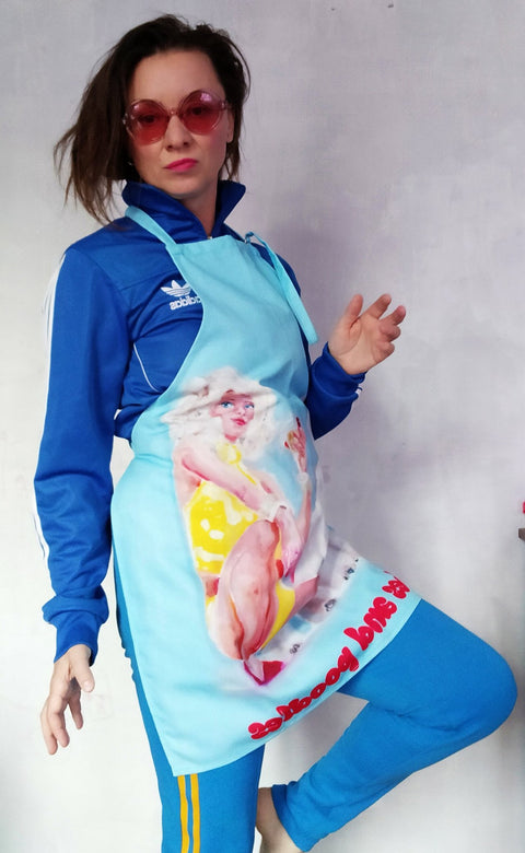 1. Woman wearing blue tracksuit and apron with pop art design of woman in yellow dress, text 'bitches and poodles'
